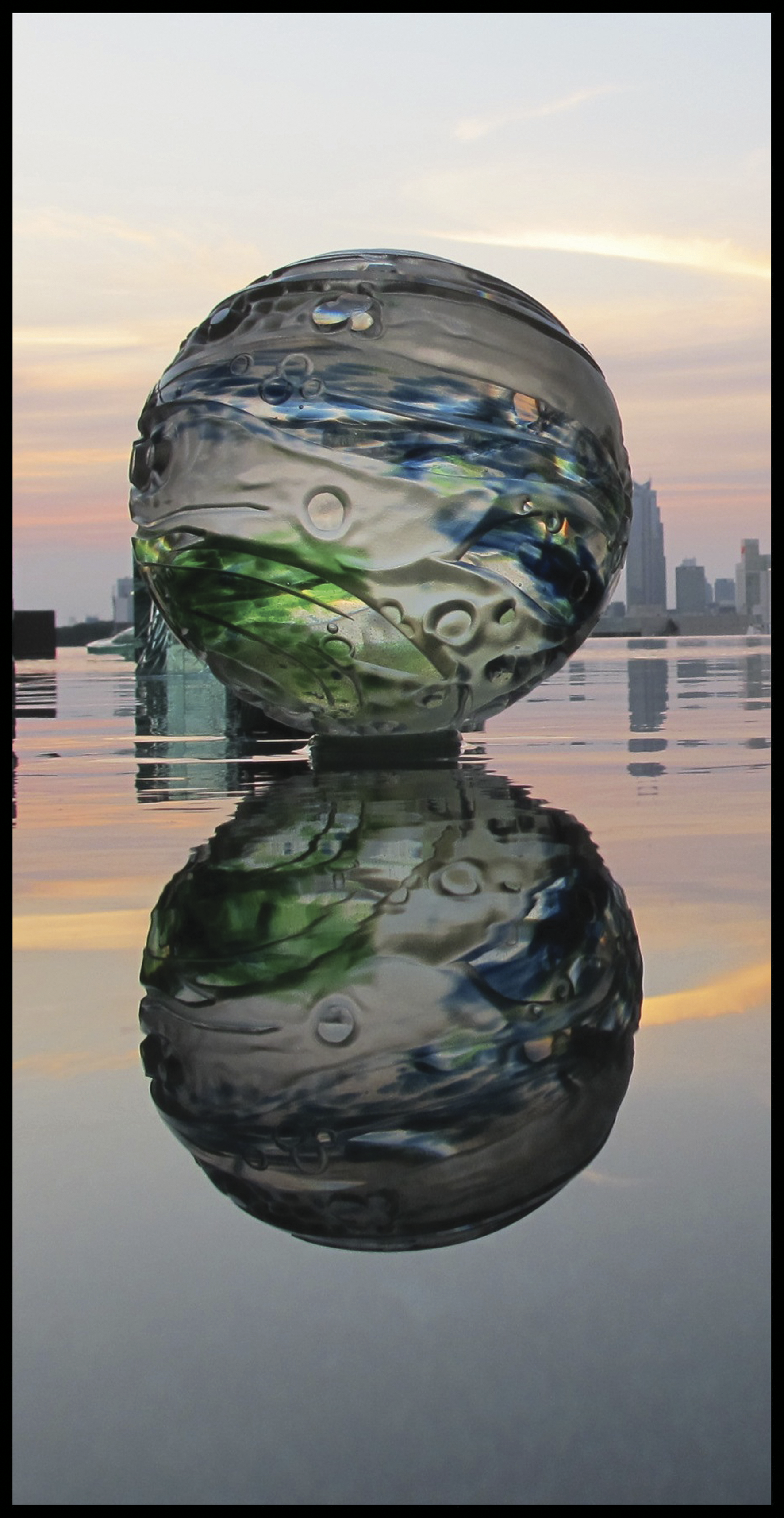 Globo de cristal soplado y tallado, instalado sobre un plano de agua con su reflejo.
